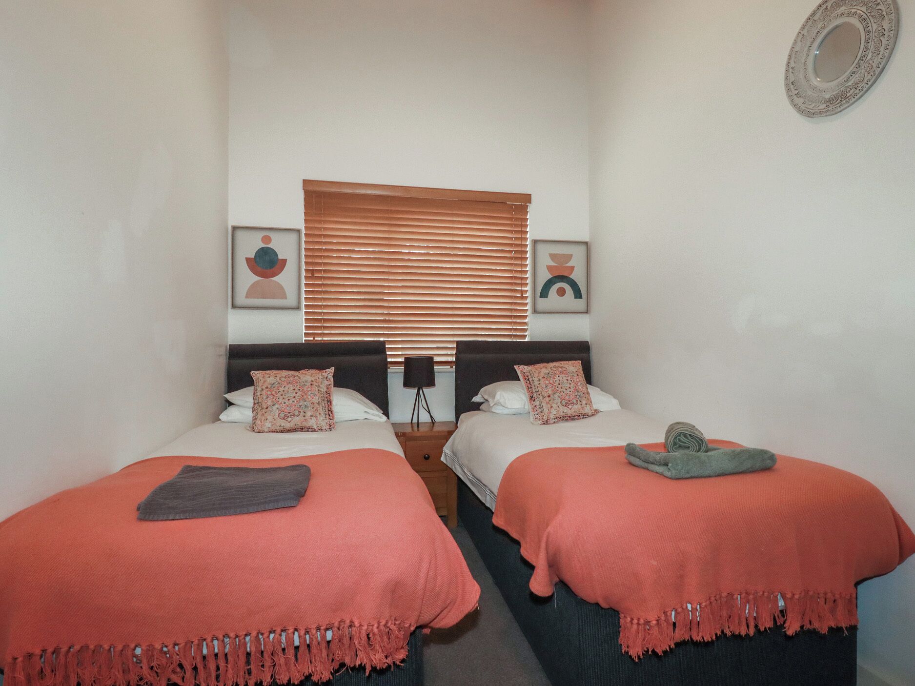 A bedroom with two beds, each with a red blanket and pillows, a wooden headboard, and a window with blinds.