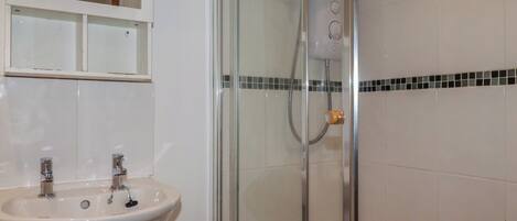 Un baño con ducha envuelta en vidrio, un lavabo blanco y un espejo sobre él.