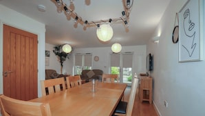 A dining area with a wooden table and chairs, a ceiling light fixture, and a wall-mounted TV. - Tregullan (Truro)