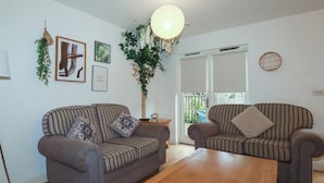 A living room with two striped sofas, a wooden coffee table, and a hanging light fixture. - Tregullan (Truro)