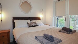 A neatly made bed with a patterned throw, a bedside table, and a wall-mounted light fixture. - Tregullan (Truro)