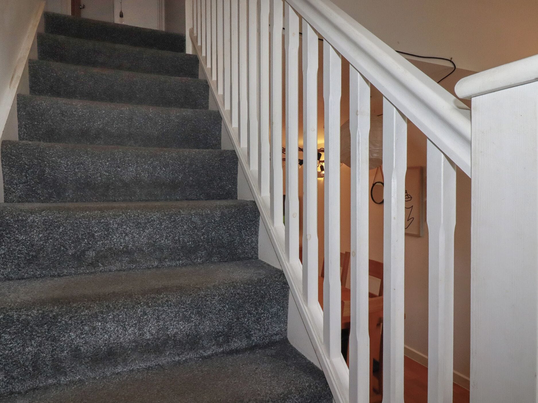A staircase with dark stone steps and white railings leading to a room with a bed and a nightstand.