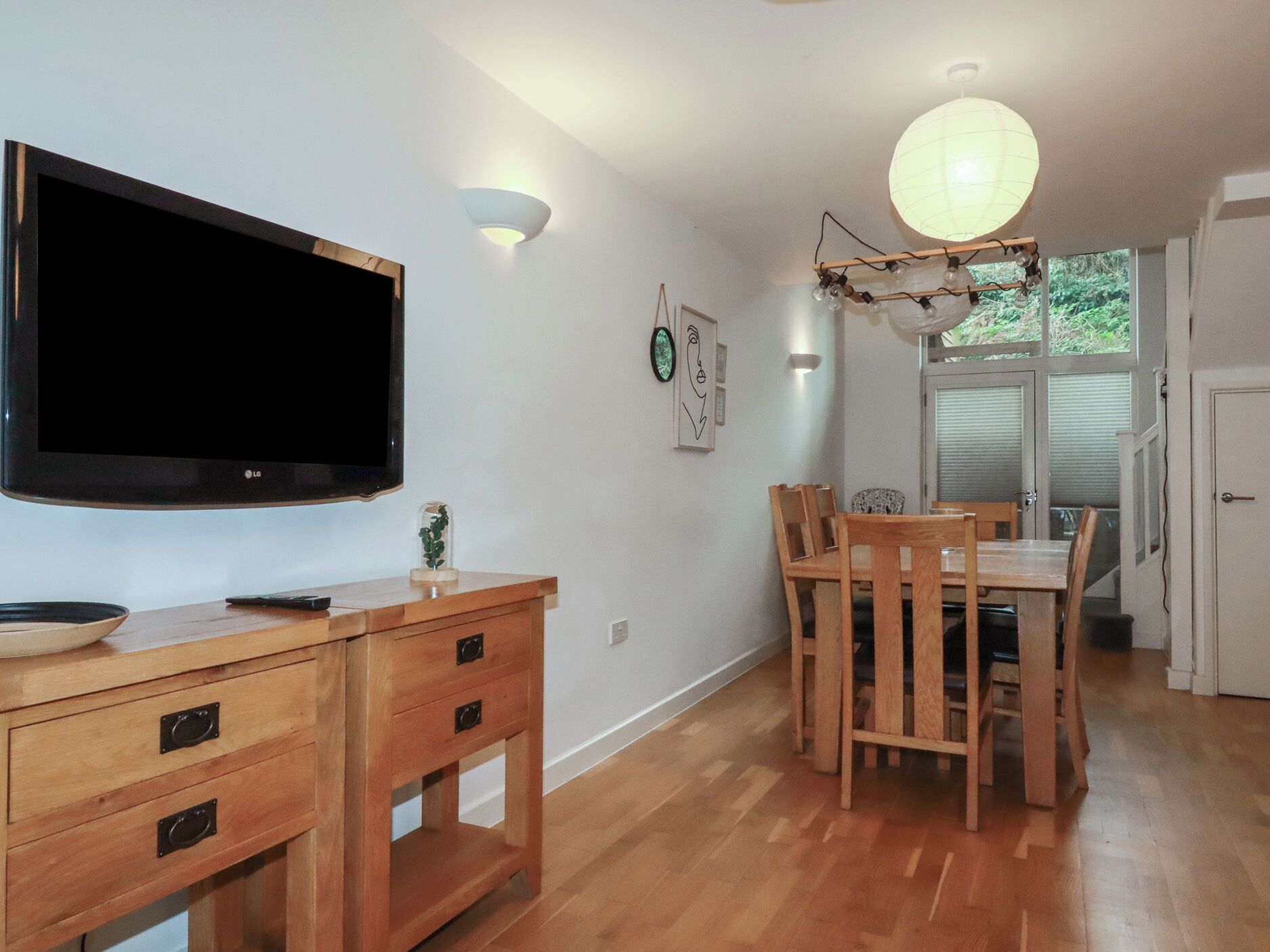 Un coin repas avec une table et des chaises en bois, un téléviseur fixé au mur et un luminaire suspendu au plafond.
