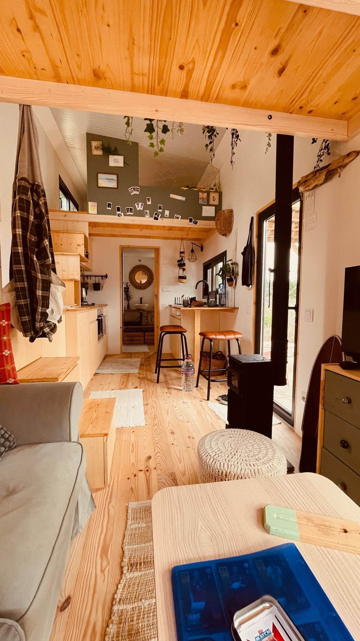 A cozy interior with a wooden ceiling, a dining area, a kitchen, and a living room with a sofa and ottoman.