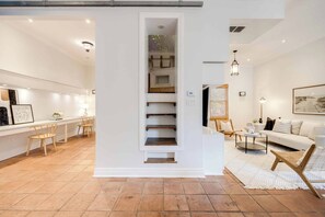 Um interior moderno com uma escada que leva a um mezanino, uma sala de jantar com cadeiras de madeira e uma sala de estar com sofá e mesa de centro.