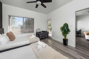 A bedroom with a bed, a desk, a chair, a large plant, and a ceiling fan.