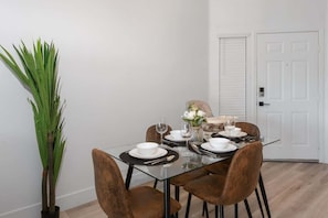 A dining area with a glass table, brown chairs, white plates, and a vase with flowers.