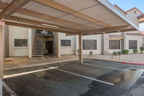 A covered parking area with a building entrance, a staircase, and a clear sky.