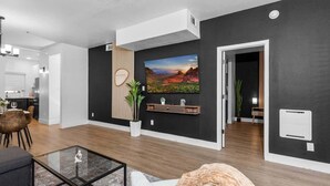 A modern living room with a large painting, a glass coffee table, and a white sofa. - Snug 2BR-Pool, BBQ,Prkng, Yoga Rm, Gym, Cabanas (Scottsdale)