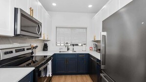 A modern kitchen with white cabinets, a stainless steel refrigerator, and a black stove. - Snug 2BR-Pool, BBQ,Prkng, Yoga Rm, Gym, Cabanas (Scottsdale)