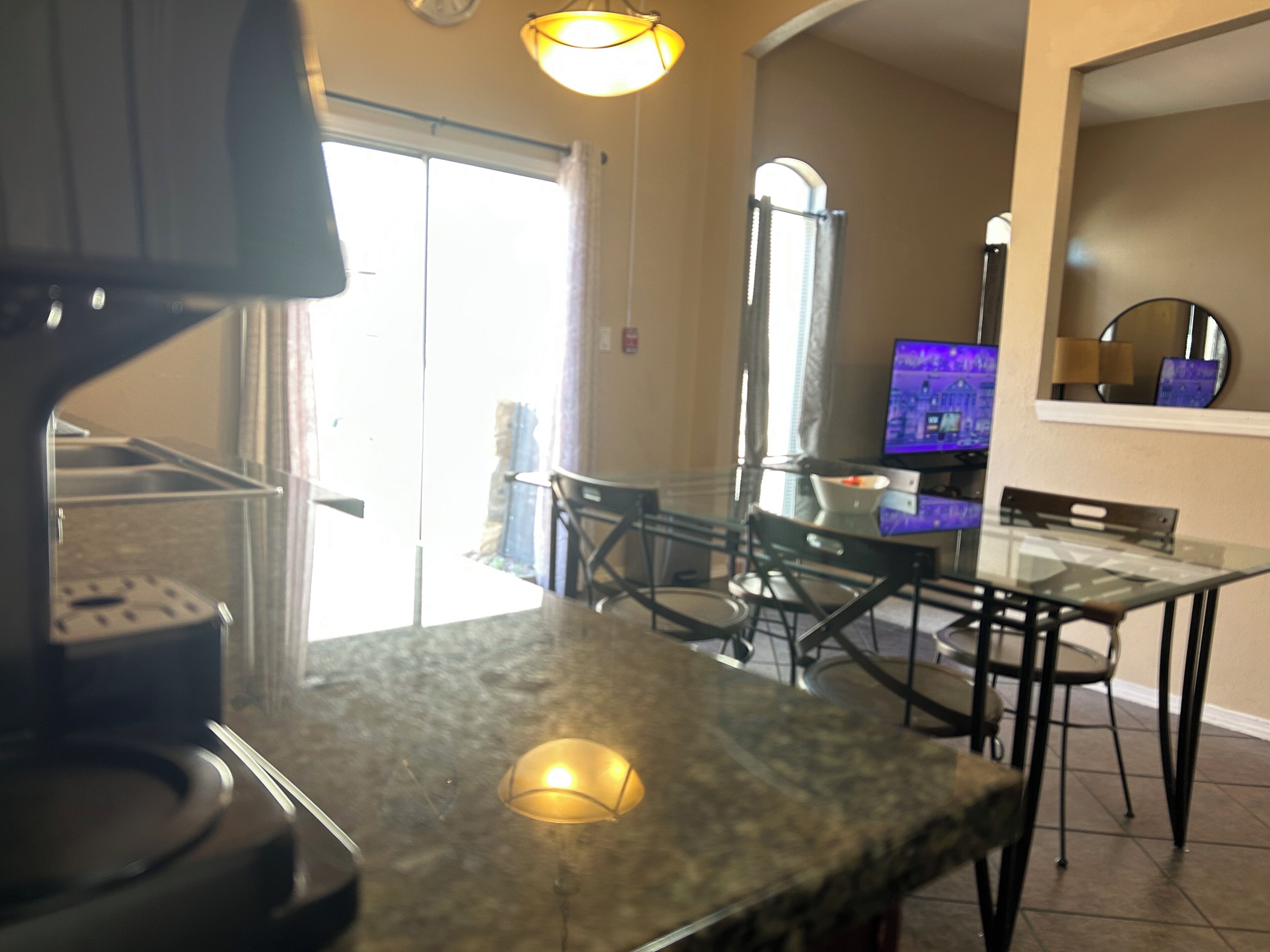 Une cuisine dotée d’un plan de travail en granit, d’une machine à café et d’un coin repas avec une table et des chaises en verre.