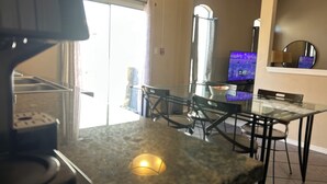 A kitchen with a granite countertop, a coffee machine, and a dining area with a glass table and chairs.