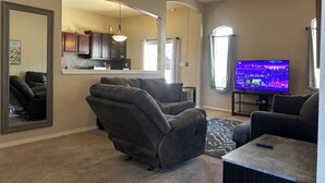 A living room with a ceiling fan, a television, and a kitchen area visible through a large mirror.