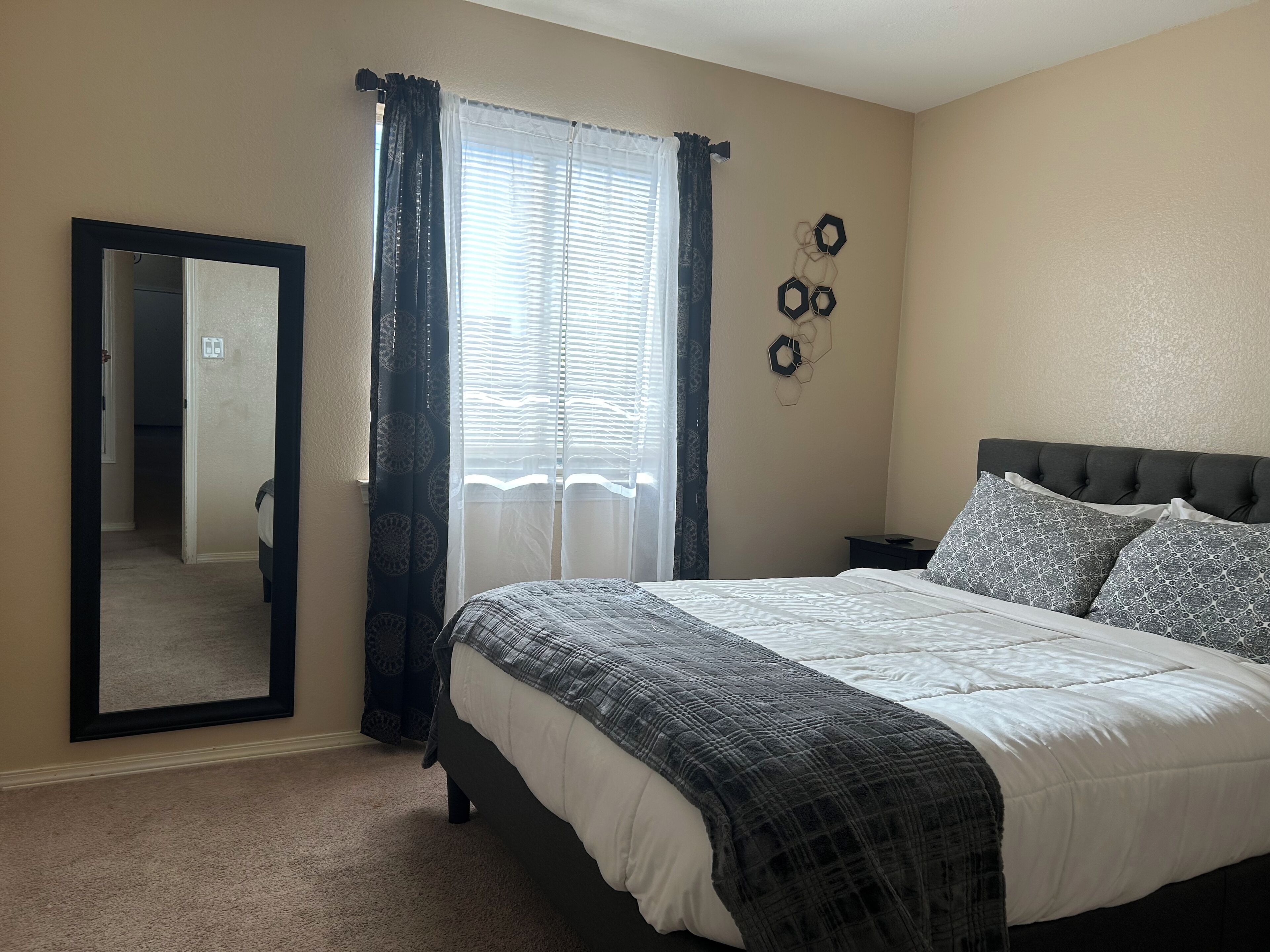 Une chambre à coucher avec un lit, un miroir, une fenêtre avec des rideaux et des éléments de décoration murale.