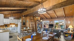 Una cocina amplia con armarios de madera, un comedor con una gran mesa de madera dispuesta para seis personas, y una sala de estar acogedora con un sofá y un televisor.