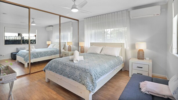 A bedroom with a large mirror, a bed with a patterned bedspread, bedside tables with lamps, and a ceiling fan.