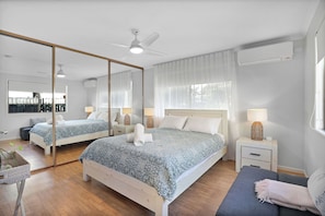 Ein Schlafzimmer mit einem großen Spiegel, einem Bett mit gemustertem Überwurf, Nachttischen mit Lampen und einem Deckenventilator.