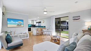 A modern living room with a sofa, a dining table with chairs, a kitchen area, and a large window with a view.