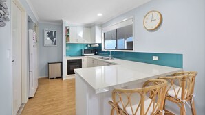 A modern kitchen with white cabinetry, a central island, a microwave, and a clock on the wall.