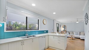 A modern kitchen with white cabinets, a large window, and a view of greenery outside.