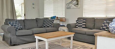 Un salon avec deux canapés gris, une table basse en bois et un tapis à motifs.