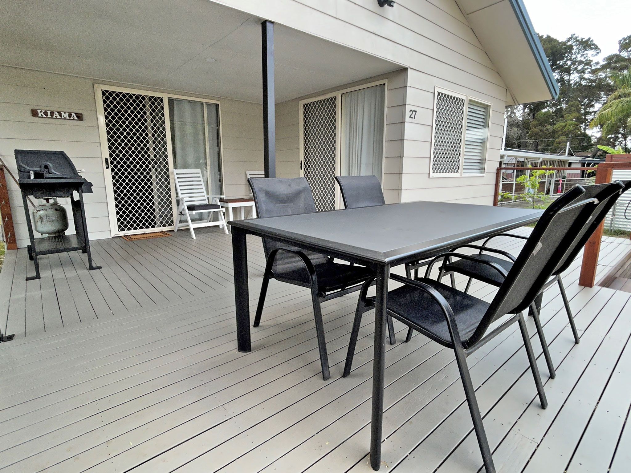 Eine überdachte Terrasse mit Tisch, Stühlen und einem Grill, sowie eine Glasschiebetür.