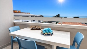 A balcony with a white table and blue chairs, overlooking a coastal view. - Seaside Retreat With Terrace in Bibione (San Michele al Tagliamento)
