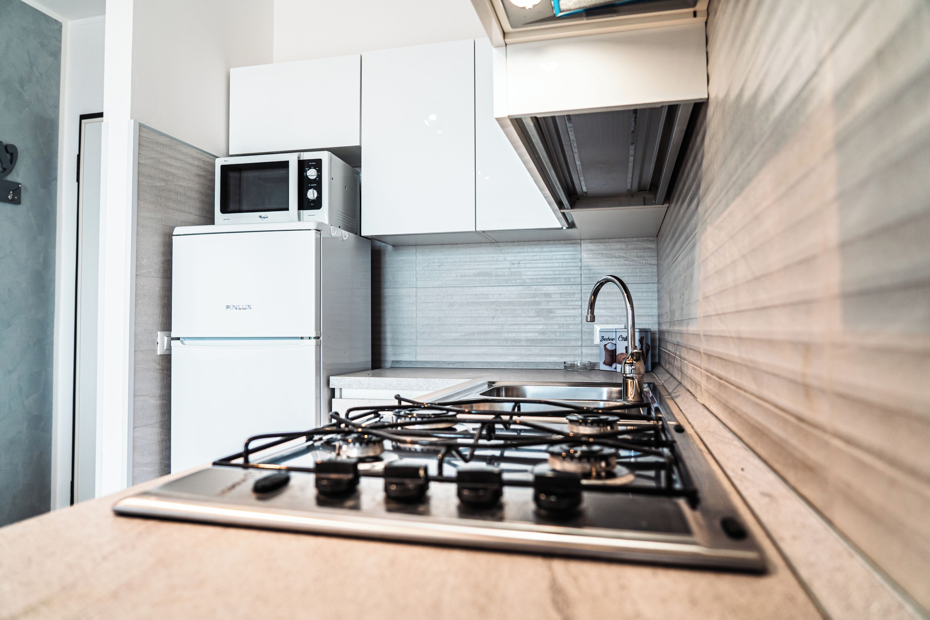 A modern kitchen with a stainless steel stove, white cabinets, and a microwave on top of a refrigerator.