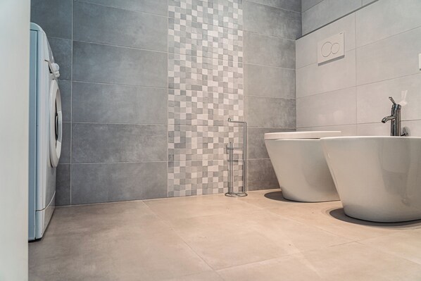 Un baño moderno con baldosas grises, un patrón de pared a cuadros, una lavadora y dos lavamanos independientes.