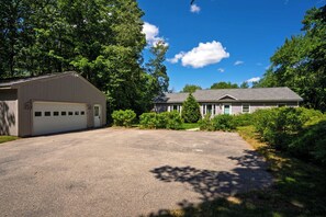 A two-story house with a garage, surrounded by lush greenery and a clear blue sky. - Single Level 4BR Pet-Friendly Home (Kennebunkport)