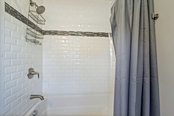 A bathroom with white subway tile walls, a bathtub, a shower with a handheld showerhead, and a grey shower curtain.