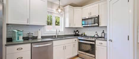 A modern kitchen with white cabinetry, stainless steel appliances, and a wooden floor.