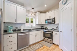 A modern kitchen with white cabinetry, stainless steel appliances, and a wooden floor. - Single Level 4BR Pet-Friendly Home (Kennebunkport)