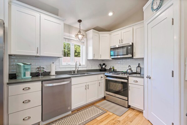 A modern kitchen with white cabinetry, stainless steel appliances, and a wooden floor. - Single Level 4BR Pet-Friendly Home (Kennebunkport)