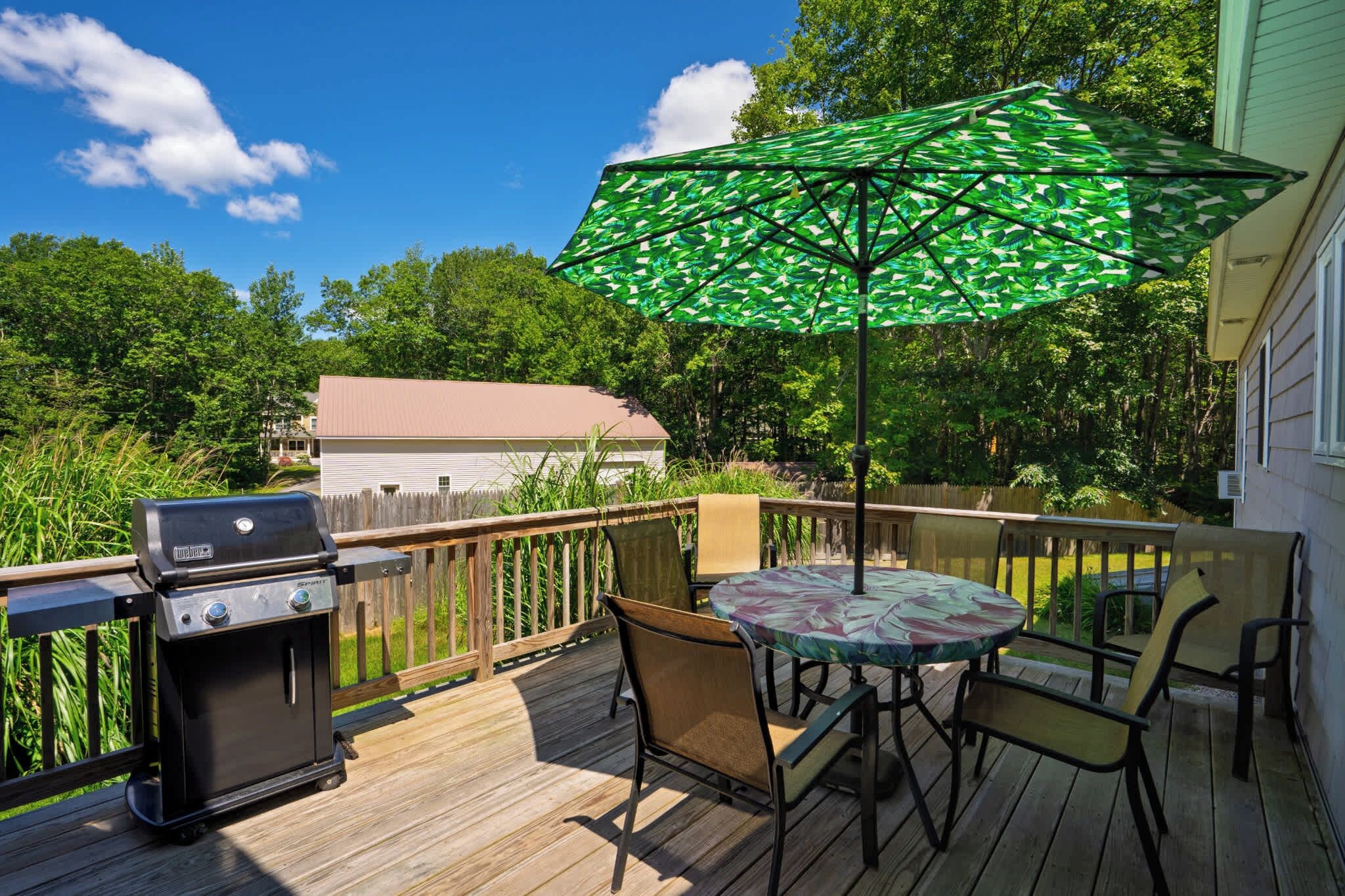 A deck with a grill, outdoor table, chairs, and a green umbrella.