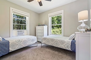 A bedroom with two beds, a dresser, a ceiling fan, and large windows with a view of trees. - Single Level 4BR Pet-Friendly Home (Kennebunkport)