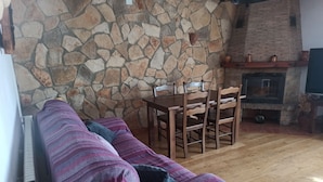 En hyggelig stue med en stenvæg, pejs, et træspisebord med stole og en stribet sofa.