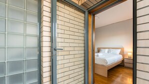 Quarto moderno com cama, mesa de cabeceira e porta de vidro que dá para uma varanda.
