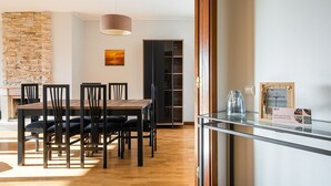 Uma sala de jantar com mesa e cadeiras de madeira, parede de pedra e luminária pendente moderna.