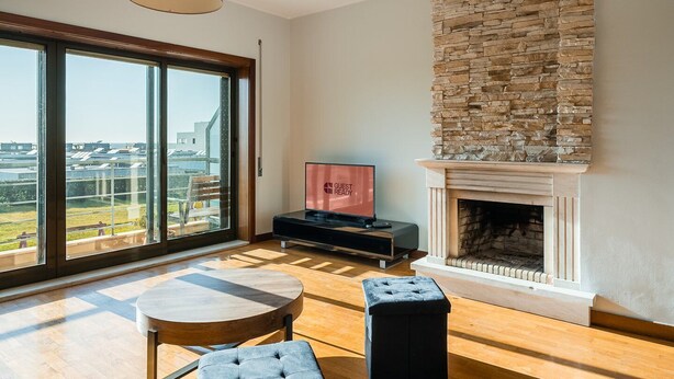 Uma sala de estar ampla com lareira, televisão e uma grande janela com vista para a cidade.