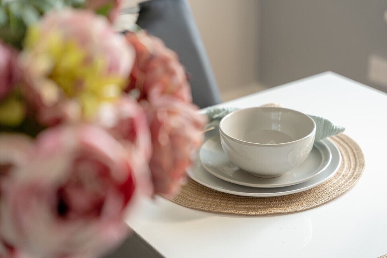 Une table blanche avec un bol et une soucoupe posés sur un set de table en fibres tressées.