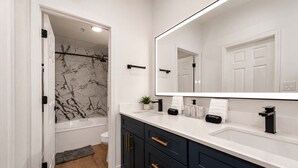 A modern bathroom with a marble shower, a large mirror, and dark cabinetry.