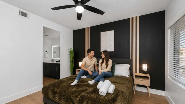 A modern bedroom with a bed, a ceiling fan, a bedside table with a lamp, and a window with blinds.