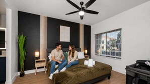 A modern bedroom with a bed, a ceiling fan, a window with blinds, and a small plant.
