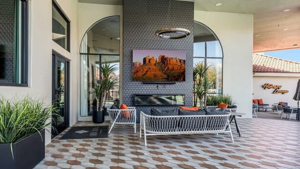 Un espacio exterior moderno con asientos, una gran pantalla de televisión, plantas en macetas y un suelo con diseño.
