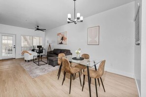 A modern living room with a glass dining table, leather chairs, a gray sofa, and a ceiling fan.