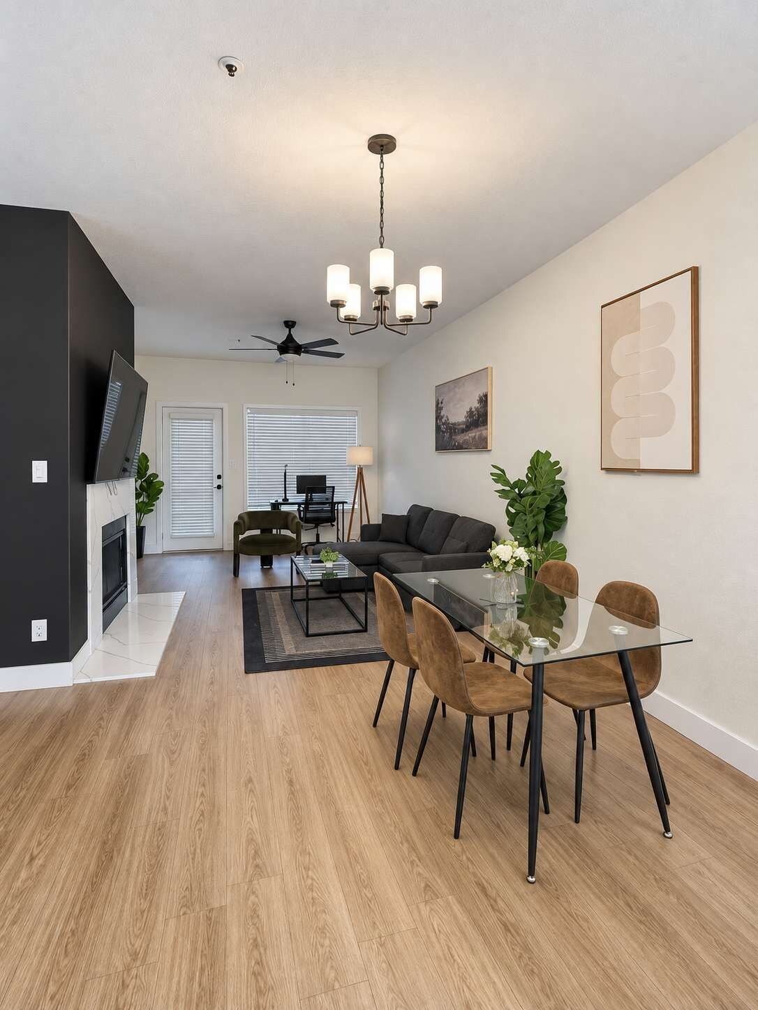 Een moderne woonkamer met een glazen eettafel, een zwarte bank en een plafondventilator.