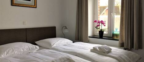 A hotel room with two beds, a window with curtains, a framed picture on the wall, and a potted orchid on the windowsill.