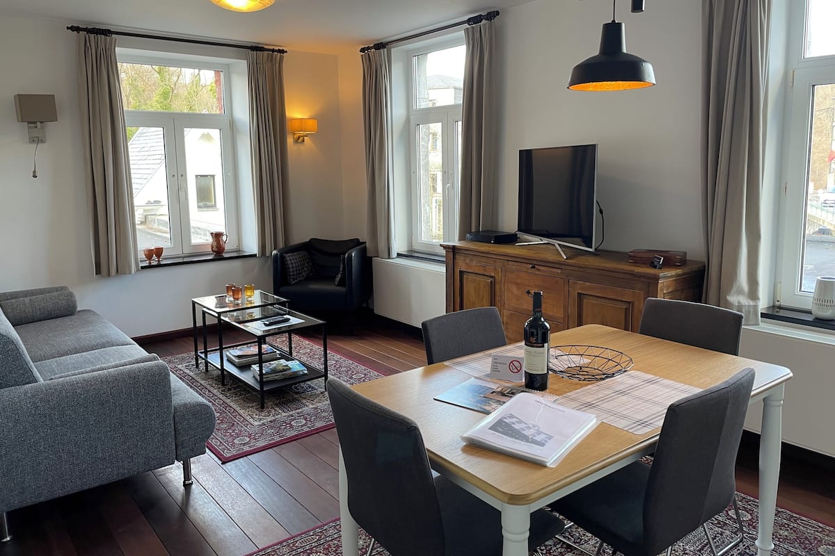 A modern living room with a sofa, a coffee table, a dining table with chairs, a TV, and a cabinet.