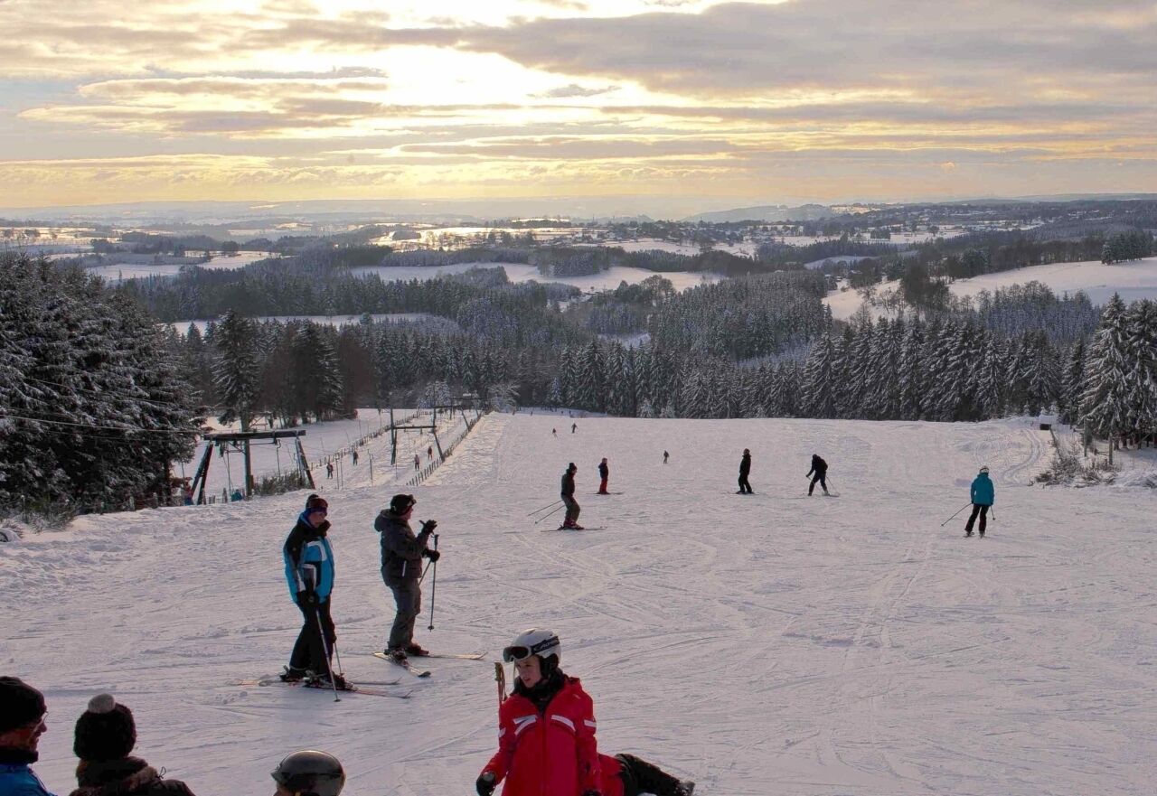 A ski slope with skiers and a clear view of the surrounding landscape.